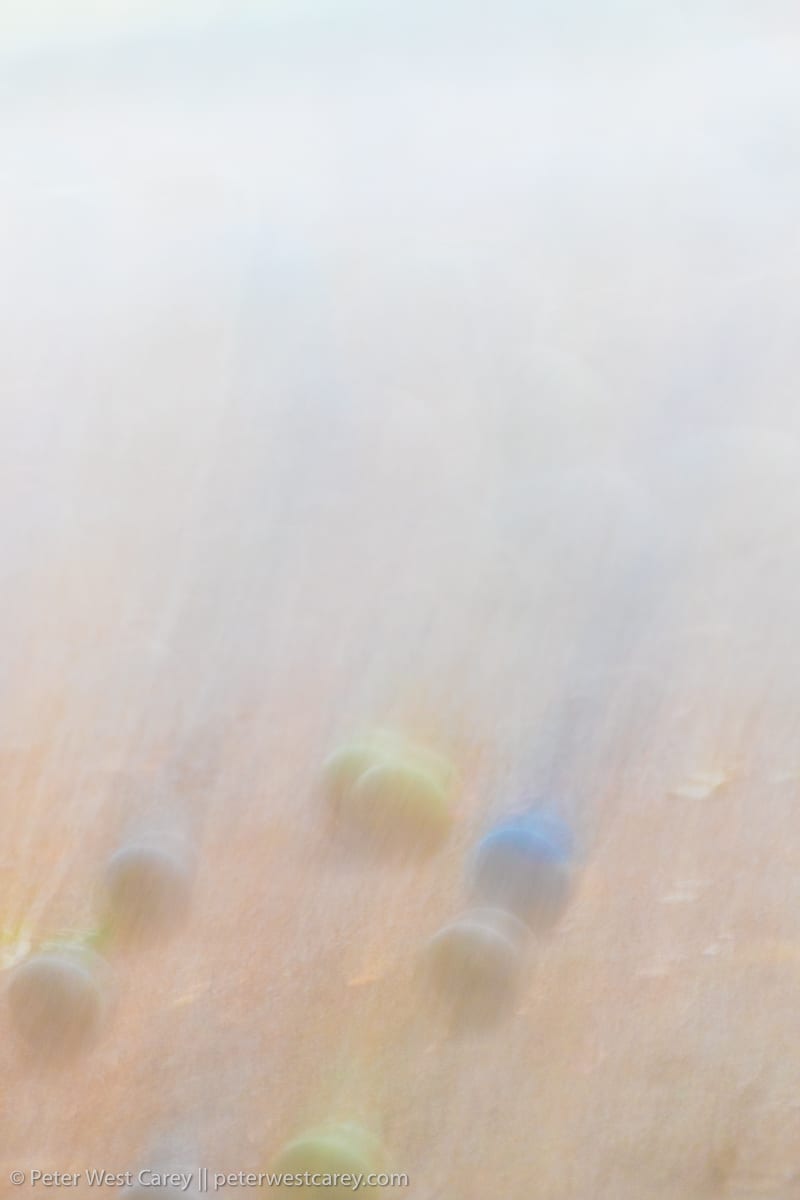 Abstracted and blurred bocce balls appear to be in motion on a sand court