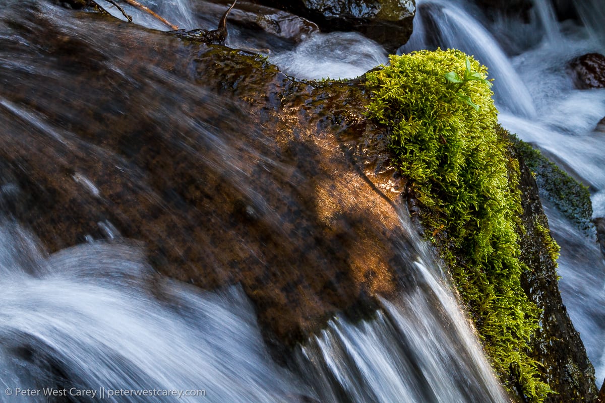 Water pours over rocks with green moss